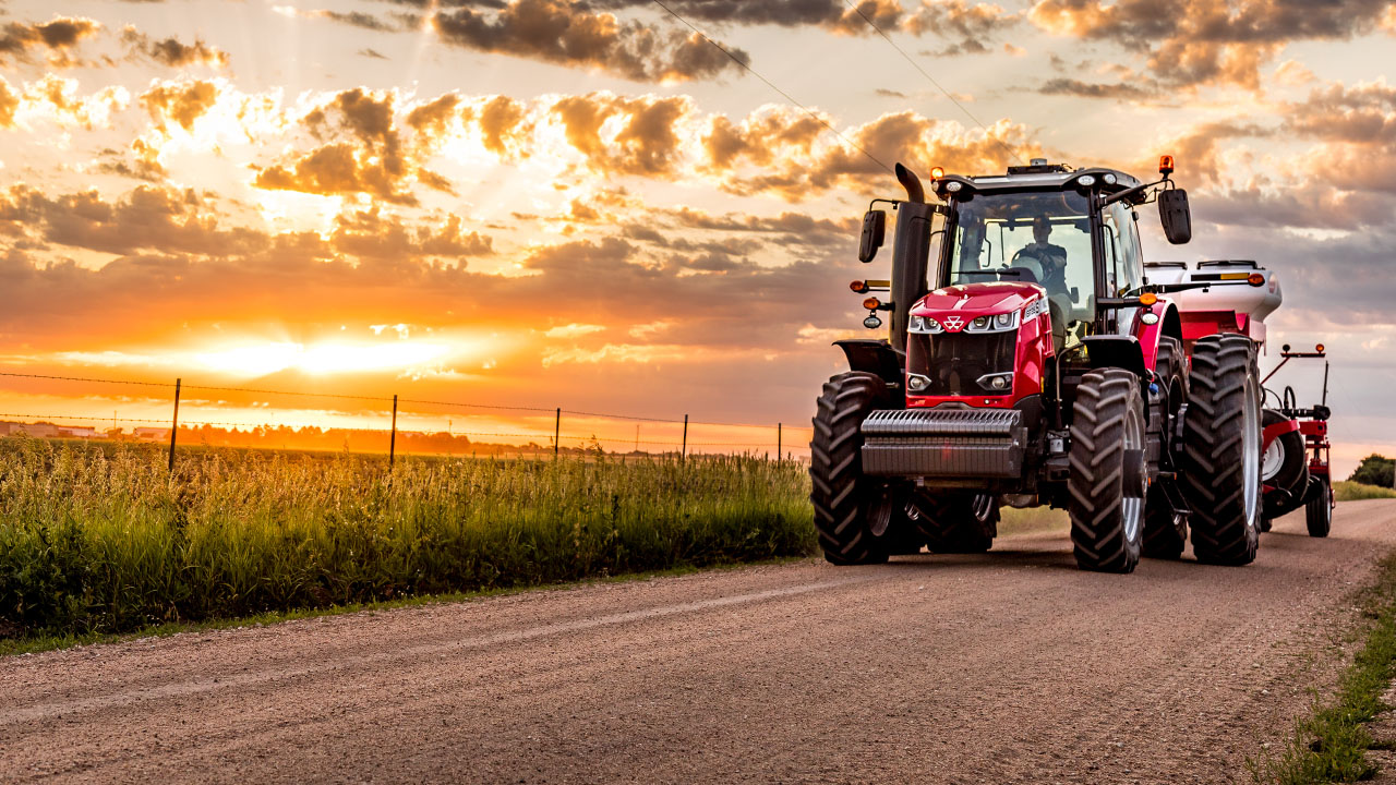 Massey Ferguson 8700S tractor hauling equipment on rural road at sunset, showcasing power and efficiency for modern farming.