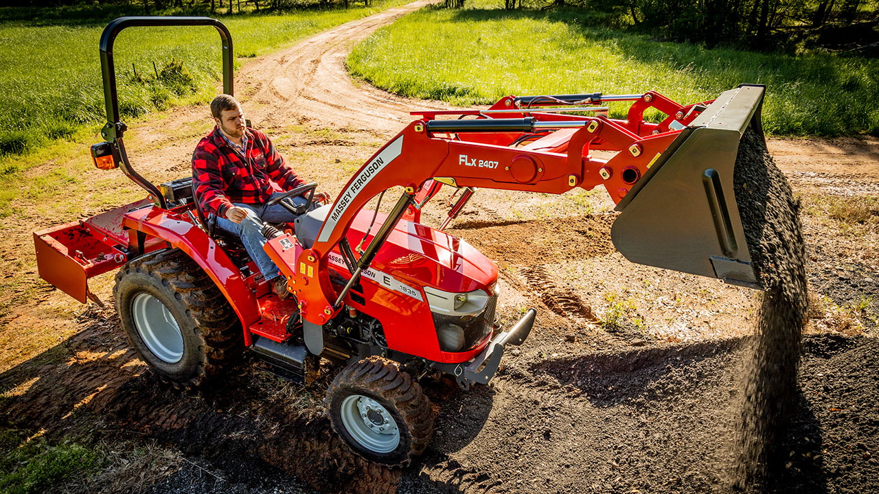 Man operating a Massey Ferguson 1800E compact tractor with front loader, spreading gravel on a rural path