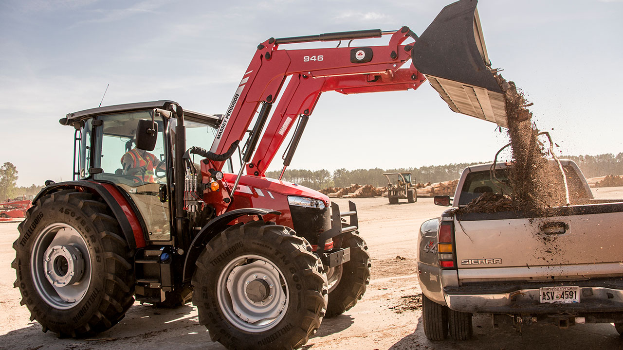 Massey Ferguson 6700 Series tractor dumping debris into truck, showcasing versatile utility and heavy-duty performance.