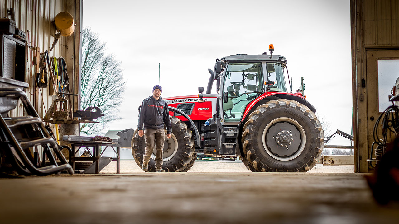 Farmer standing in front of a Massey Ferguson 7S Series tractor parked outside a farm workshop.