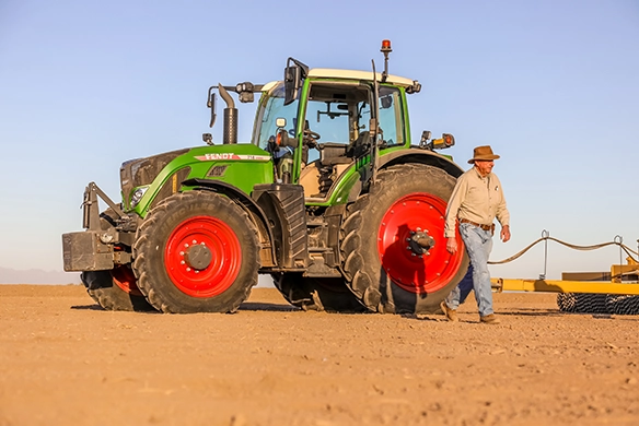 Farmer walking away from his Fendt 700 Vario on a dusty field under a pale blue sky.