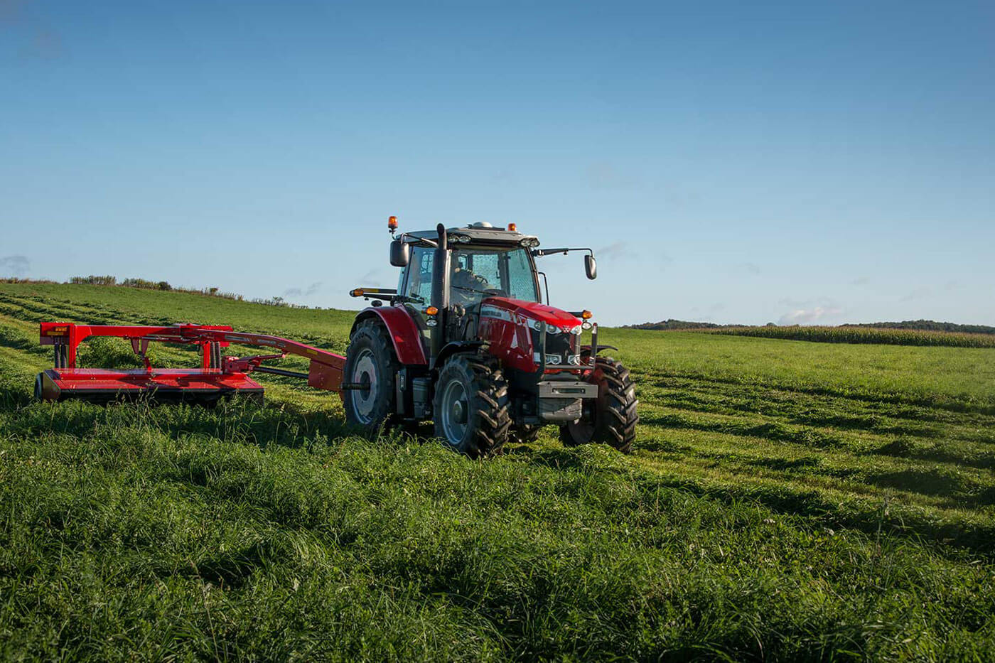 Massey Ferguson 1300 Series mower conditioner cutting hay in a large green field, pulled by a MF tractor.