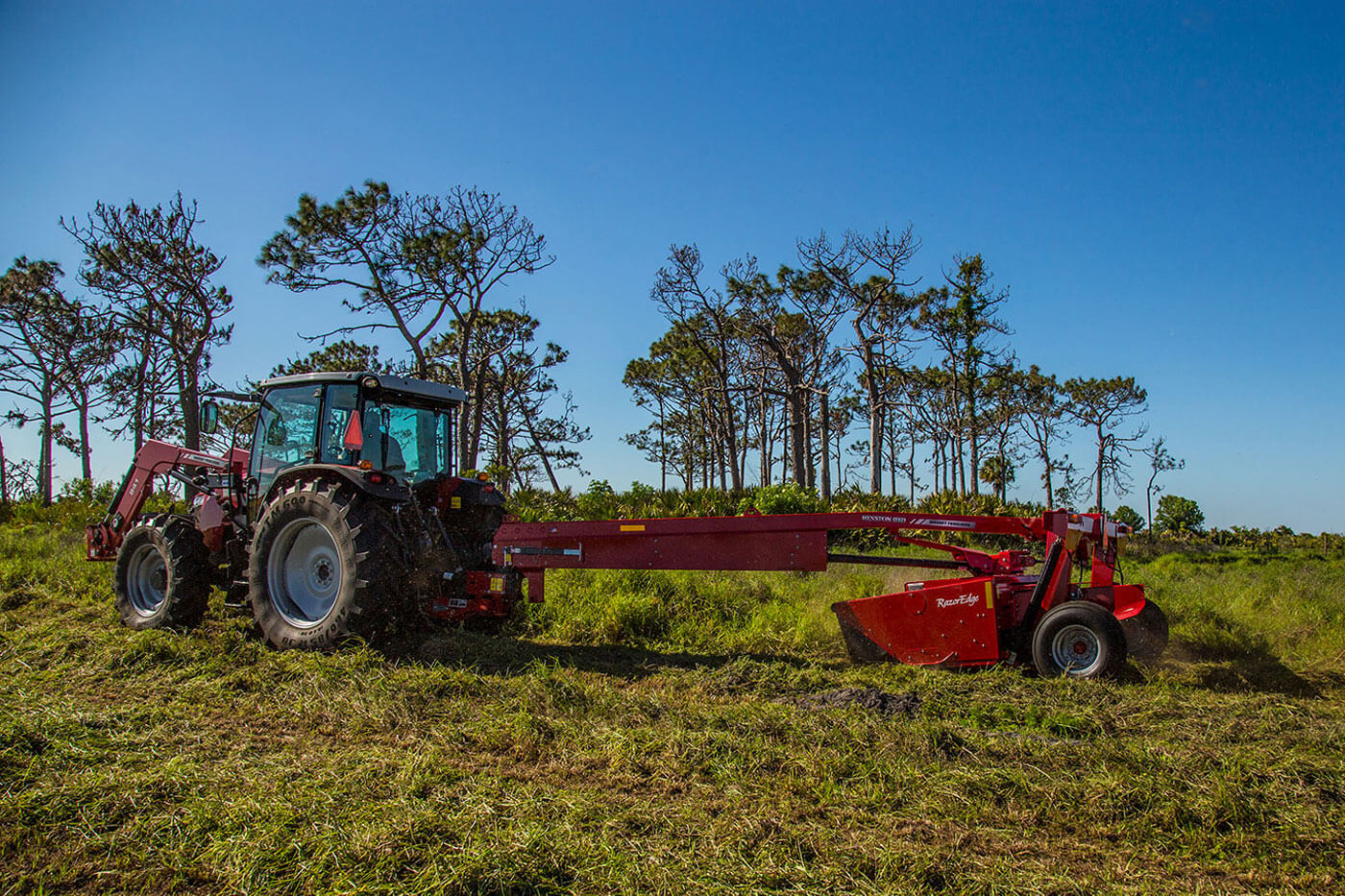 Massey Ferguson 1300 Series mower conditioner cutting grass in open field, towed by a MF tractor with front loader.