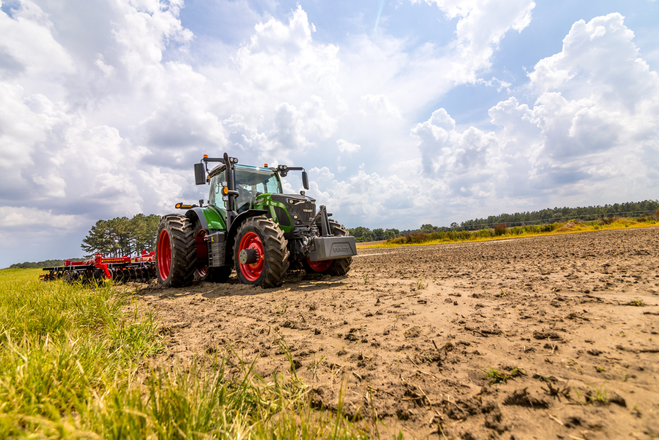 Fendt 600 Vario tractor pulling Sunflower tillage equipment across a field under a partly cloudy sky.