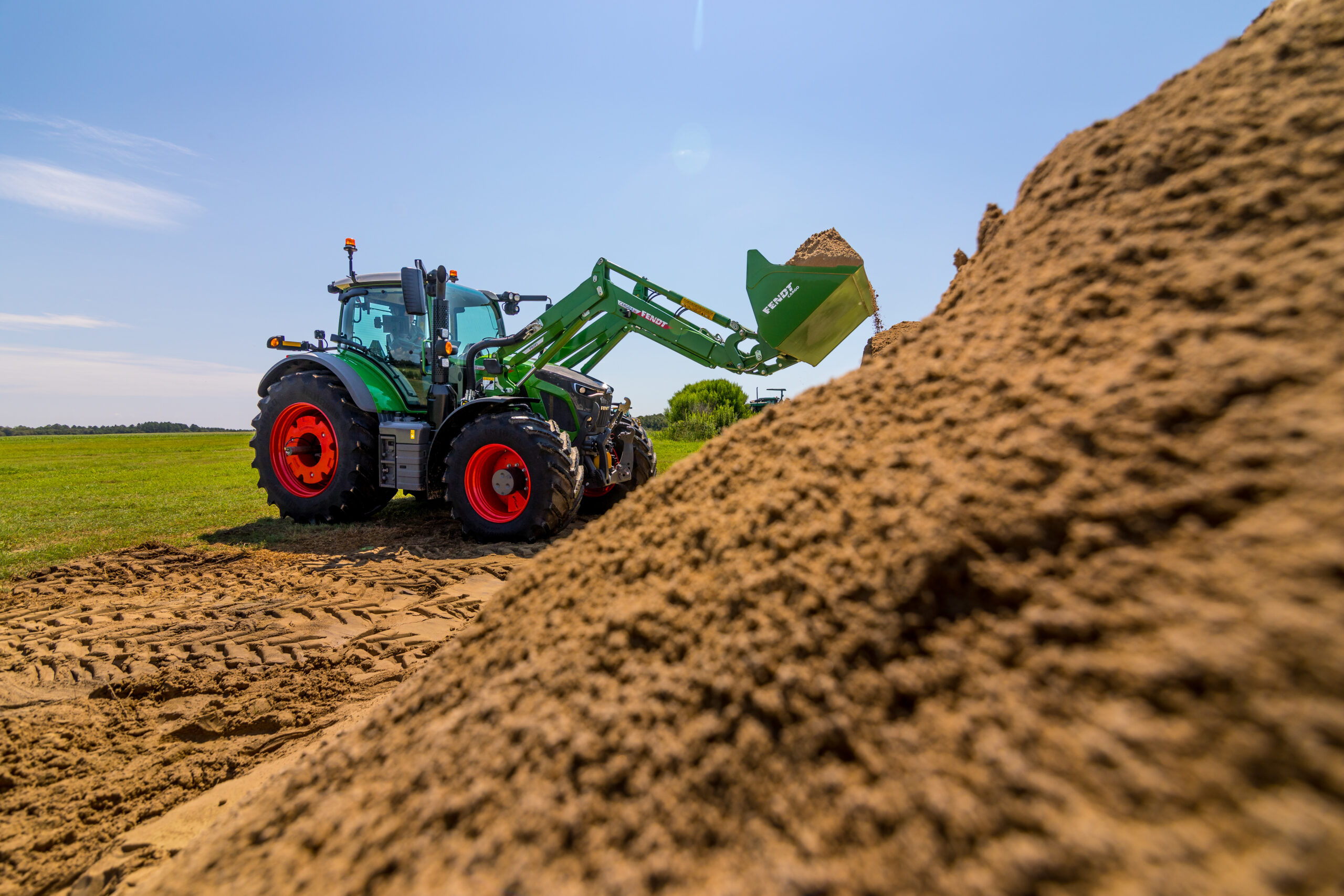Fendt 600 Vario tractor with front loader moving soil on jobsite under clear blue sky.