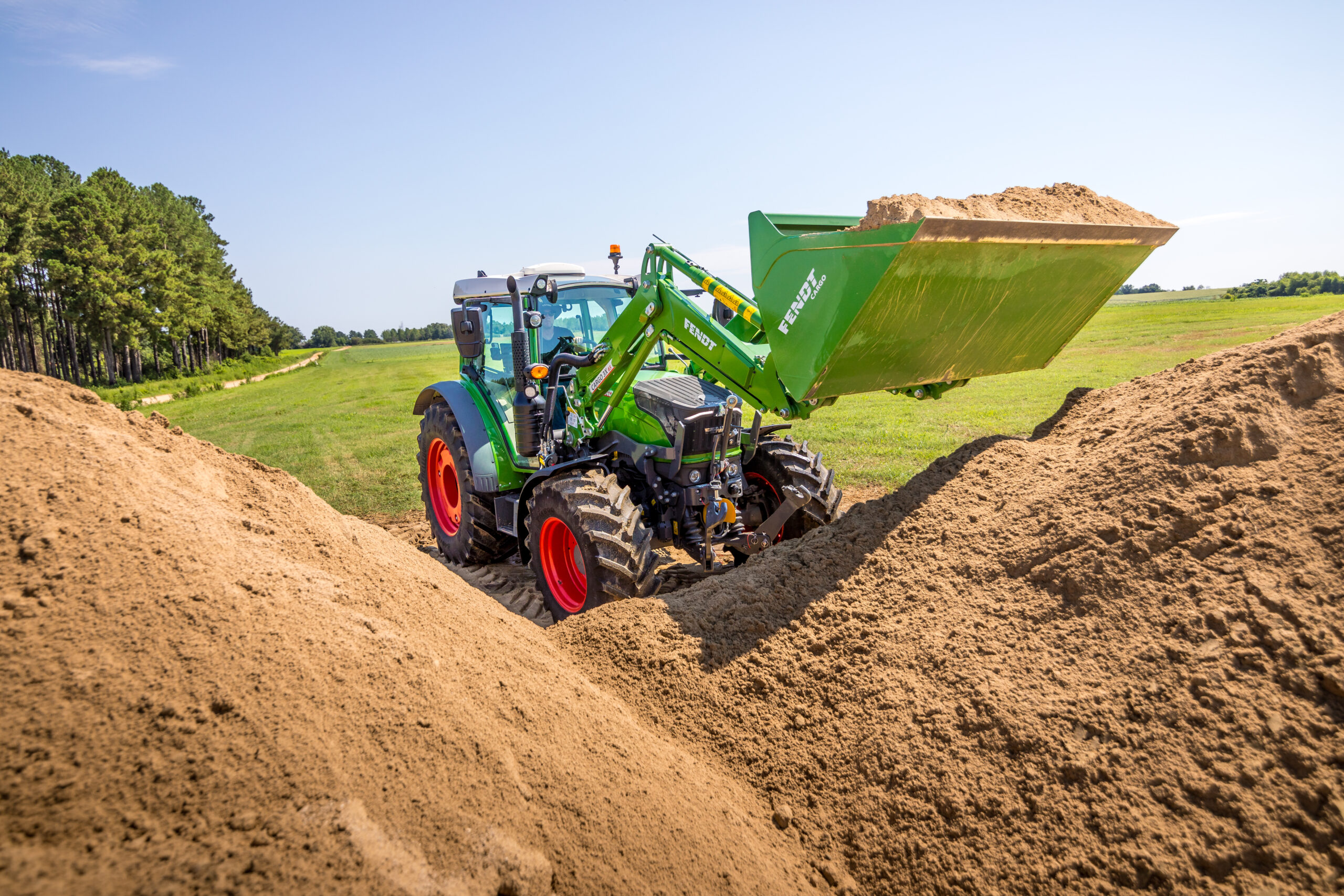 Fendt 200 Vario tractor with front loader moving sand on open farmland, showcasing agility and versatility.