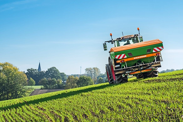 Amazone ZA-TS precision fertilizer spreader mounted on a Fendt tractor working across a sloped green field with optimal spread control.