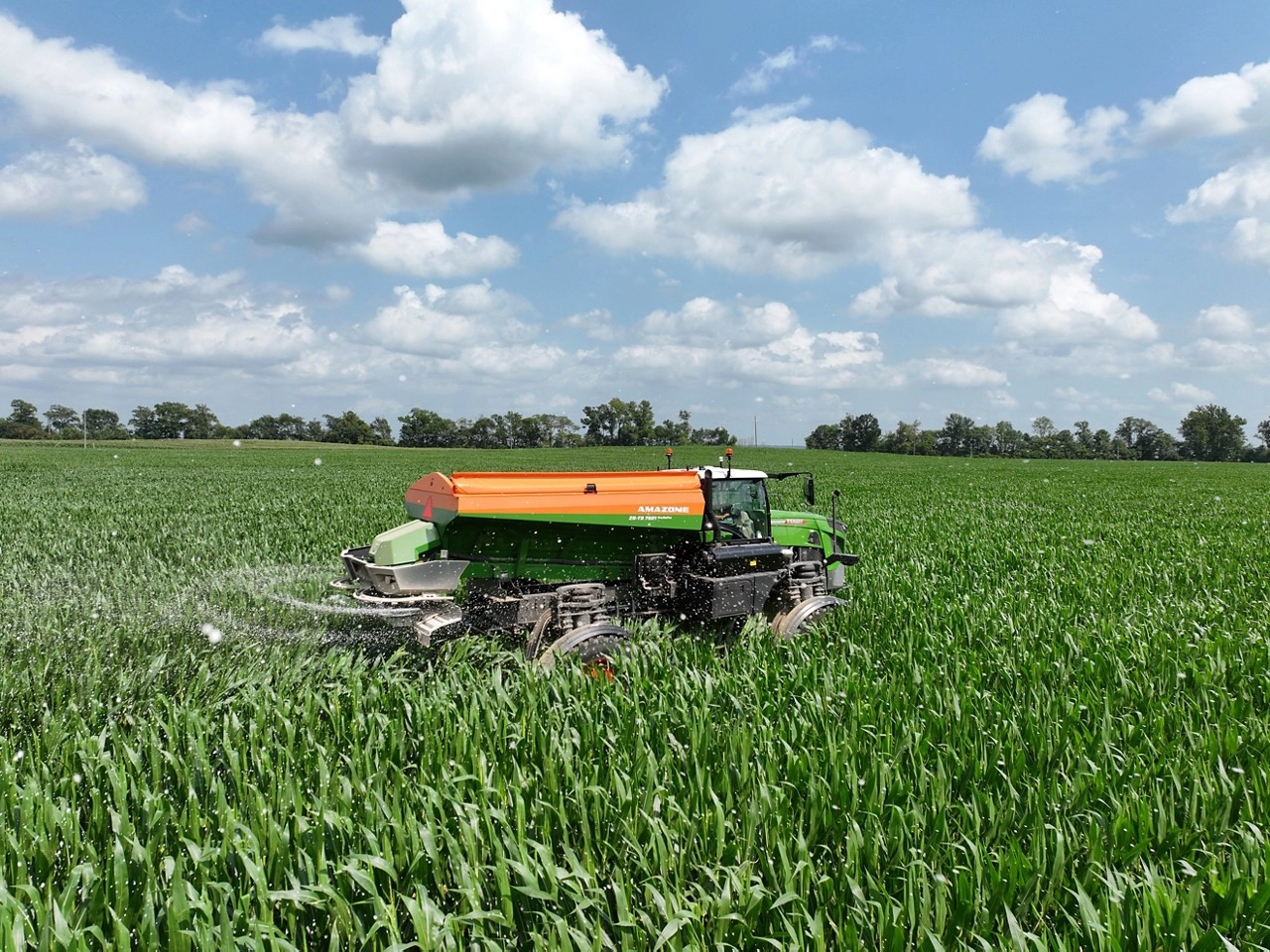 Fendt Rogator with Amazone ZG-TS spreader operating in a tall, green crop field, effectively applying nutrients under a bright sky for optimal yield results.