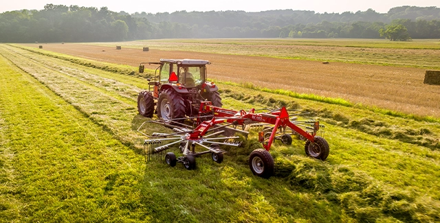 Massey Ferguson 5700 Global Series tractor pulling a Massey Ferguson RK 662 rotary rake through a field of forage for hay production.