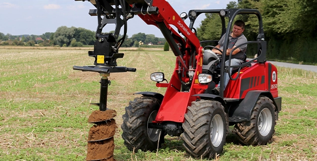 Schäffer 3650 series compact loader with auger drilling a hole for a fence post.