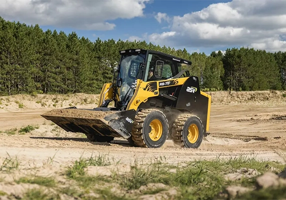 ASV RS-75 skid steer loader moving dirt on a sandy jobsite, equipped with rugged tires and a front loader bucket.