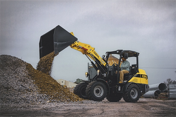 Operator using a Gehl AL550 articulated loader to move a pile of gravel at a construction site, showcasing compact design and maneuverability.