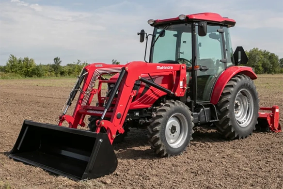 Mahindra 2600 series red utility tractor equipped with a front loader, parked on a tilled field ready for work.