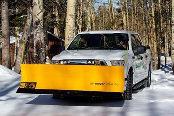 White pickup truck equipped with a Meyer Drive Pro yellow snow plow clearing a snowy path in a wooded area.