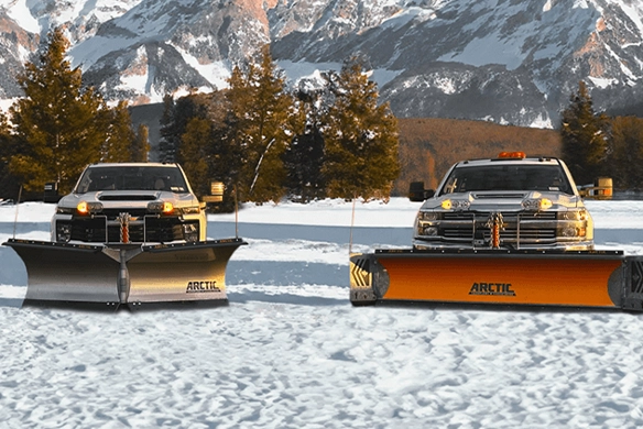Two trucks fitted with Arctic brand snow plows working in a snowy area with a scenic mountain backdrop