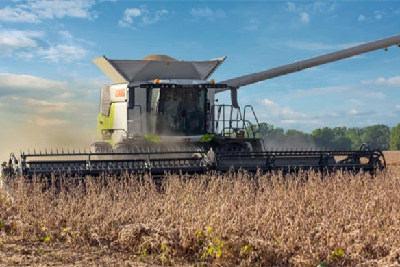 CLAAS TRION 740 combine harvesting soybeans using a wide draper header, actively unloading grain into a waiting trailer in the background.