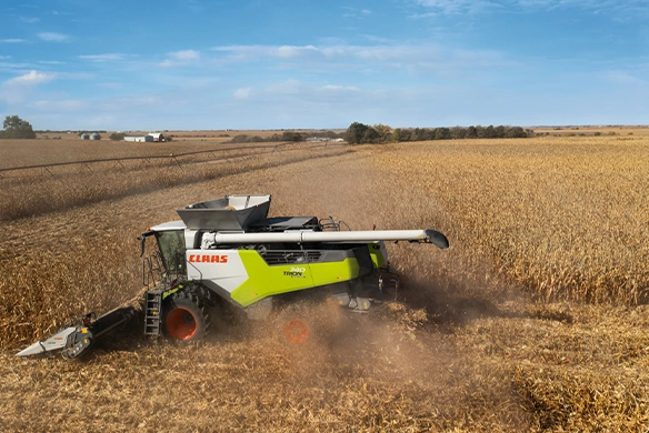 CLAAS TRION 740 combine with auger folded cutting through corn on flat terrain, leaving a clear harvest trail and dust plume behind.