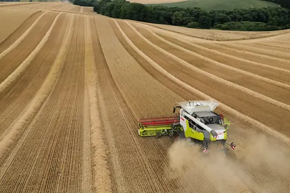 Aerial view of CLAAS TRION 740 combine harvesting wheat across contour rows in a large field, demonstrating efficient ground coverage.