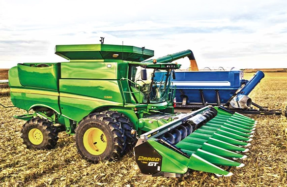 Drago GT Series corn head mounted on a John Deere S680 combine, unloading into a blue grain cart during harvest operations.