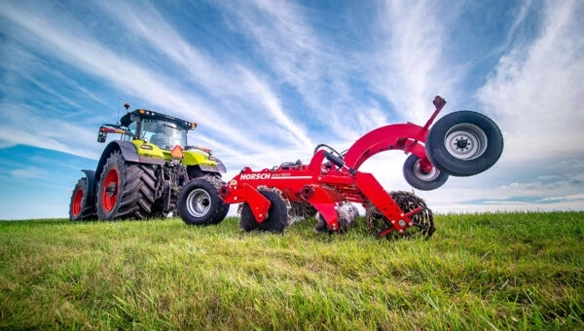 CLAAS tractor towing a HORSCH Joker RX cultivator across a grassy field, showcasing durable tillage performance and heavy-duty frame design.