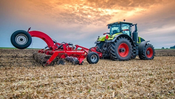 CLAAS tractor working a cornfield with a HORSCH Joker RX cultivator during sunset, highlighting residue incorporation and consistent tillage depth.