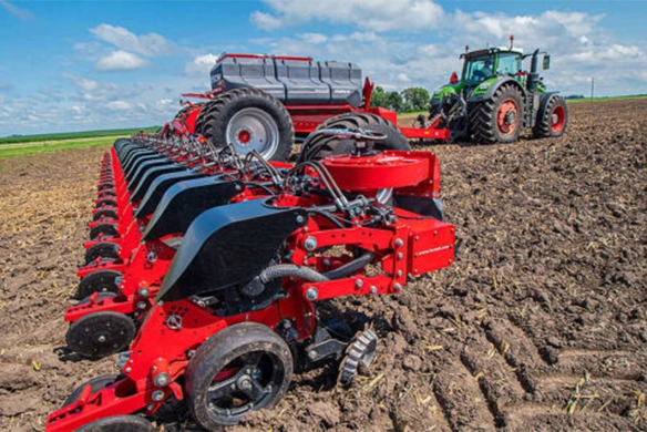 Close-up view of a HORSCH Maestro planter attached to a Fendt tractor, planting in neat rows across a tilled field under a bright blue sky.
