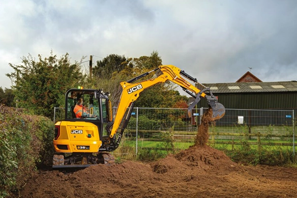 JCB 35Z-1 mini excavator digging and moving soil at a farm site, operated by a worker in a high-visibility jacket.
