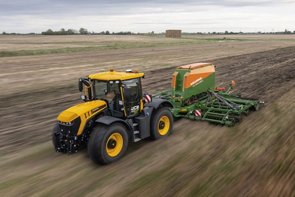 JCB Fastrac 4220 iCON tractor towing an Amazone seed drill across a large agricultural field under cloudy skies.