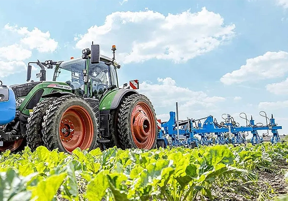 Side view of a Fendt tractor pulling a LEMKEN implement across a green field, demonstrating advanced crop cultivation equipment.