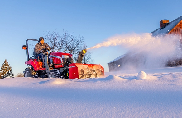 Massey Ferguson 1GC Series compact tractor with front snow blower clearing deep snow at sunrise.