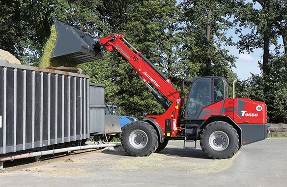 Schäffer 9660 T telescopic loader unloading silage into a high-sided container using extended boom reach.