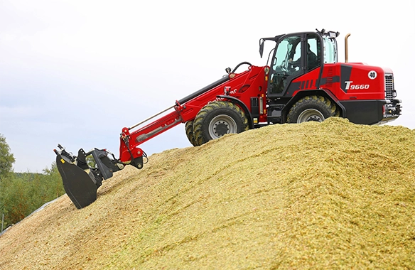Schäffer 9660 T telescopic loader using a grapple bucket to manage silage on top of a mound, showing full reach extension.