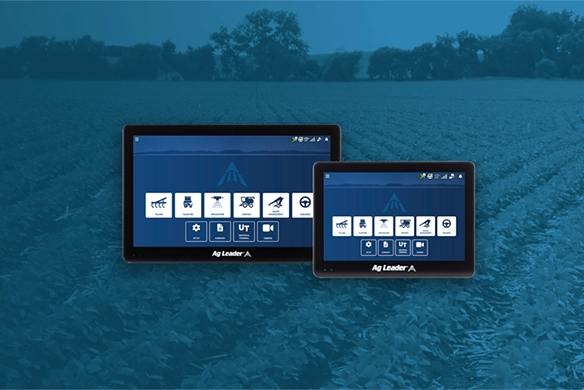 Two Ag Leader touchscreen displays showing precision farming system icons, overlaid on a background image of a growing crop field.