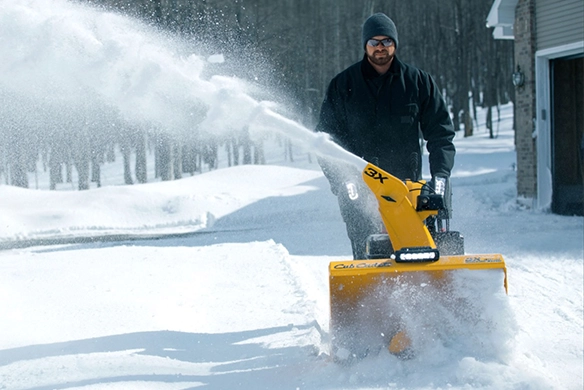 Person using a Cub Cadet snow blower to clear a driveway in winter