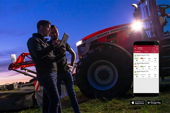 Two farmers stand beside a Massey Ferguson tractor at dusk, using a tablet to review machine data, with a mobile app interface shown on screen.