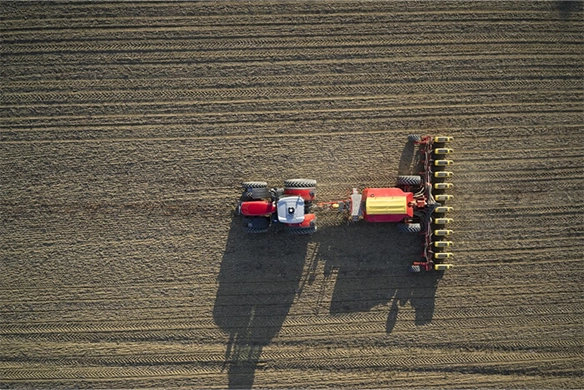 Top-down view of a Massey Ferguson tractor with precision planting equipment working in a freshly tilled, uniform field.