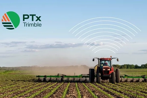 A red tractor equipped with precision ag technology works in a planted field under a clear sky, with wireless signal graphics symbolizing data connectivity and PTx Trimble logo.