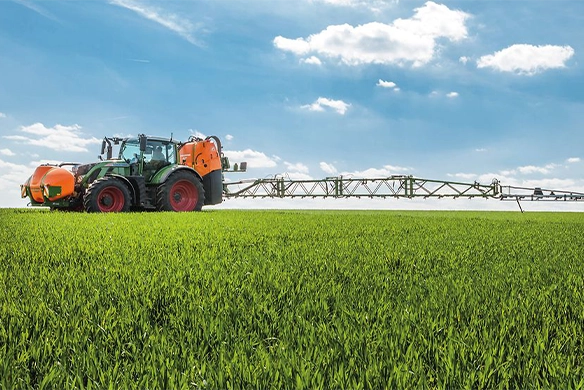 Fendt tractor spraying a lush green crop field using an Amazone UF1201 mounted sprayer and FT 1001 front tank with extended boom arms, under a bright blue sky.