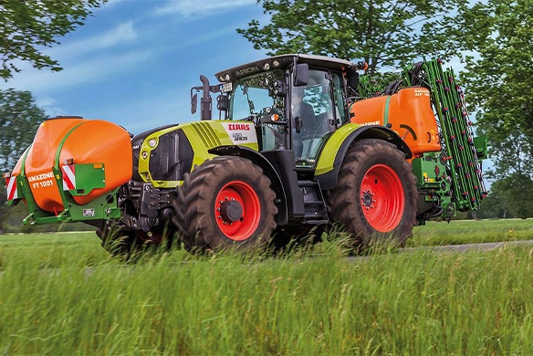 Claas tractor equipped with Amazone UF-01 mounted sprayer and FT 1001 front tank driving through a grassy field.