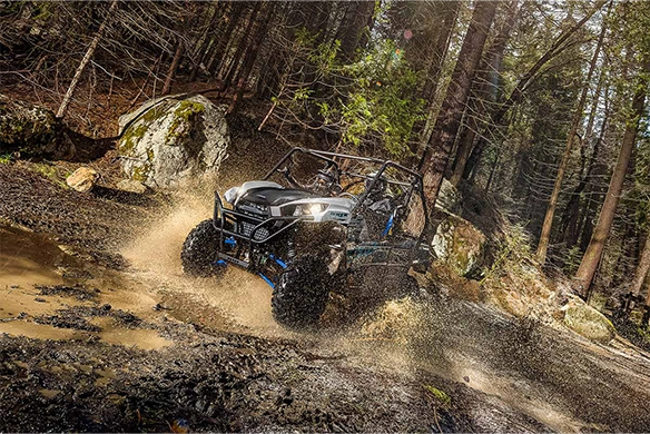 Kawasaki Teryx side-by-side vehicle splashing through muddy forest terrain