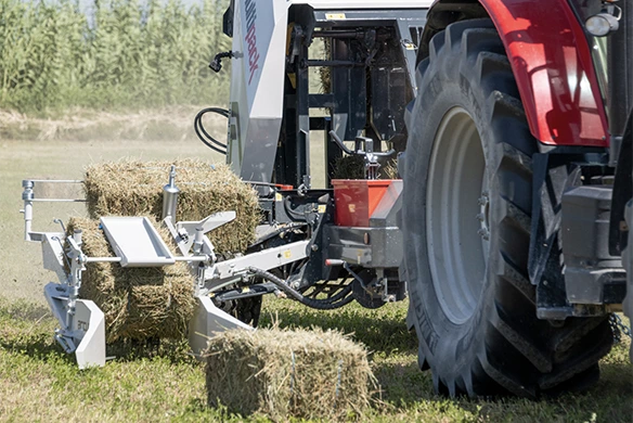 Close-up of Arcusin Multipack D14 picking up square hay bales behind a red tractor.