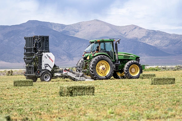 Arcusin bale bundler working in open field with a tractor collecting and bundling small hay bales.