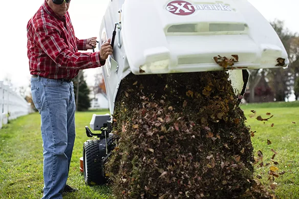 Exmark Navigator mower dumping collected leaves from rear hopper onto grass field.
