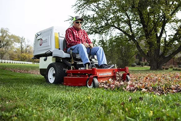 Operator using Exmark Navigator zero-turn mower to clear leaves on a residential lawn.