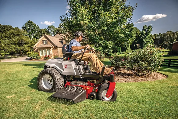 Operator using an Exmark Quest zero-turn mower for residential lawn care with precision cutting around landscape features.