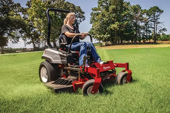Woman mowing grass with an Exmark Radius zero-turn mower in a large open field.