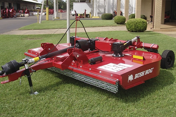 Bush Hog multi-spindle rotary cutter on grass outside a dealership building.