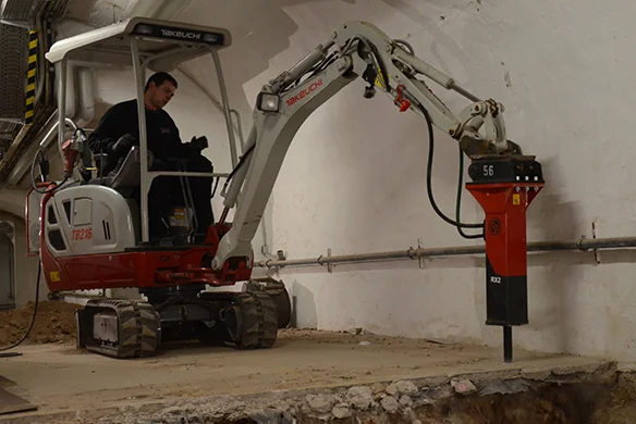 Takeuchi TB216H mini excavator equipped with hydraulic breaker for controlled indoor demolition work.