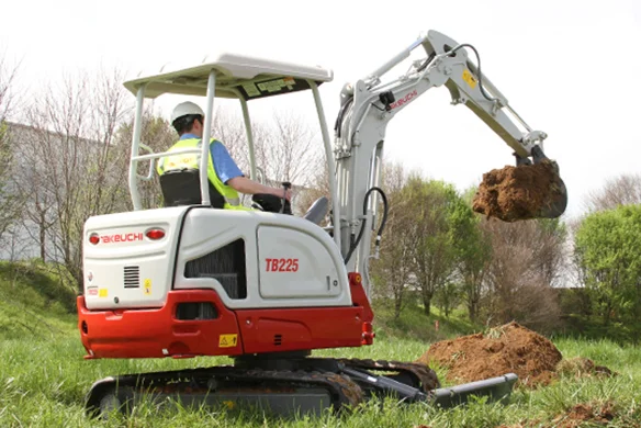 Operator using Takeuchi TB225 compact excavator to move dirt on grassy jobsite.