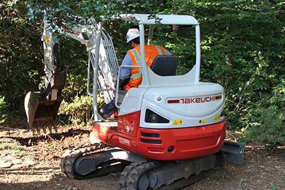 Takeuchi TB225 compact excavator clearing brush and trees in wooded worksite.